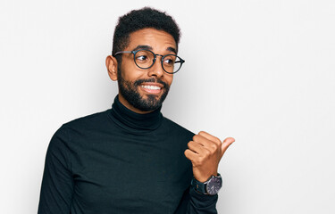 Canvas Print - Young african american man wearing casual clothes smiling with happy face looking and pointing to the side with thumb up.