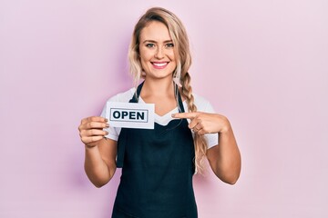 Poster - Beautiful young blonde woman wearing waitress apron holding open banner smiling happy pointing with hand and finger