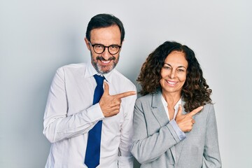 Canvas Print - Middle age couple of hispanic woman and man wearing business office uniform cheerful with a smile of face pointing with hand and finger up to the side with happy and natural expression on face