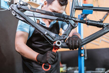 A Young Mechanic Wears Gloves Using A Bottom Bracket Wrench To Lock While Working In A Workshop