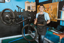 Bicycle Mechanic In Smiling Apron Holding Bicycle With Thumbs Up While Standing Beside Bicycle In Workshop