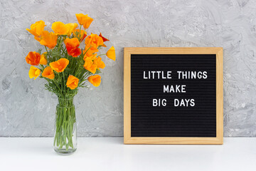 Wall Mural - Little things make big days. Motivational quote on letter board and bouquet orange flowers on white table against grey stone wall. Concept inspirational quote of the day