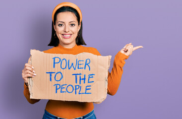 Young hispanic girl holding power to the people banner smiling happy pointing with hand and finger to the side