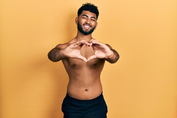 Canvas Print - Arab man with beard wearing swimwear shirtless smiling in love doing heart symbol shape with hands. romantic concept.