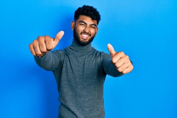 Canvas Print - Arab man with beard wearing turtleneck sweater approving doing positive gesture with hand, thumbs up smiling and happy for success. winner gesture.