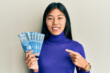 Sticker - Young chinese woman holding 10000 chilean pesos smiling happy pointing with hand and finger