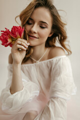 Wall Mural - Happy young girl with curly hair in summer white blouse posing with bright tulips on isolated background. Photo of pretty lady in light outfit..