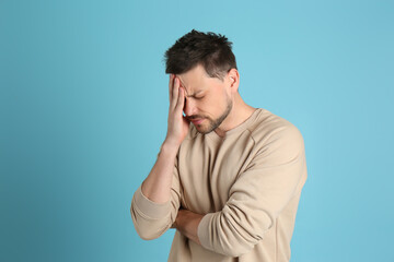 Wall Mural - Man suffering from terrible migraine on light blue background