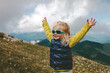 Toddler happy raised hands hiking in mountains family travel vacations healthy lifestyle 2 years old child outdoor having fun