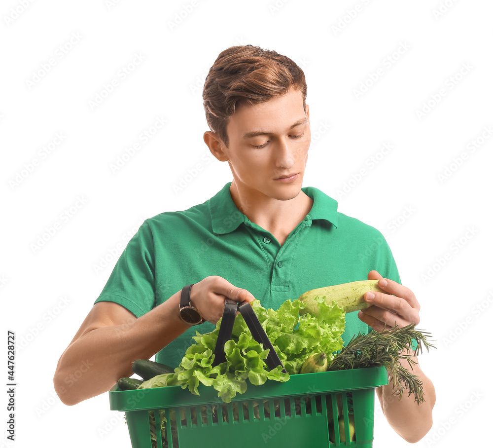 Young man holding shopping basket with fresh vegetables on white background