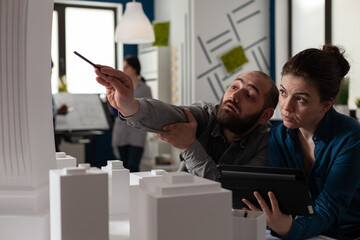 Poster - Team of construction architects work on tablet at office to plan building model maquette. Caucasian engineering partners pointing at layout project to design modern digital blueprint