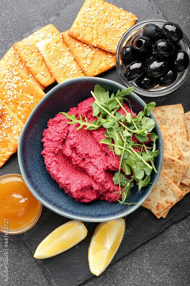 Composition with tasty beet hummus, crackers, olives and sauce on dark background, closeup