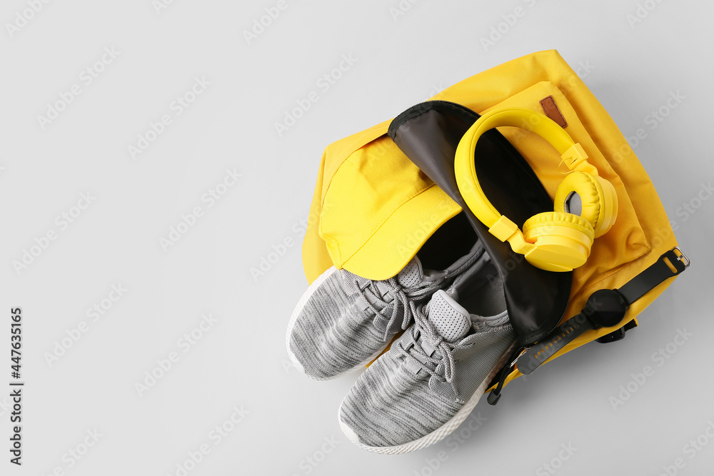 Backpack with sport shoes, headphones and smart watch on grey background - obrazy, fototapety, plakaty 