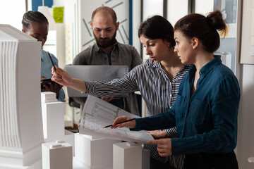 Poster - Team of diverse architects discussing blueprint plans on paper laptop computer tablet. Professional workers analyzing maquette building model for project design and construction