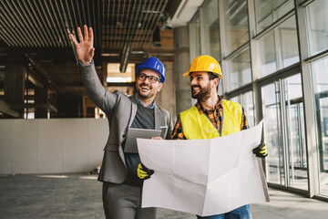 smiling architect holding tablet and showing to construction worker something he imagined. construct