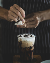 Unrecognizable Barista Carefully Decorating Creamy Foam Of Iced Coffee By Using Toothpick To Draw Chocolate Patterns Onto It Like Spider Net To Make It Look More Attractive To Be Drunk.
