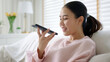© ChayTee - Asia young people teen happy girl sit relax call use smart phone talk chat send text to 5G wifi mic VoIP deep tech ai bot app at home sofa couch. Enjoy vocal order to help chatbot iot on social media.