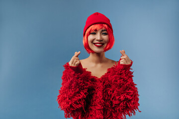 Beautiful stylish asian woman with trendy makeup and short bright hairstyle in modern cap and warm red sweater smiling and looking into camera..