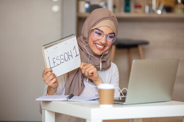 Side view head shot smiling mixed race lady freelancer wearing headset, communicating with client via video computer call. Muslim pleasant professional female tutor giving online language class