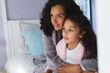 © Wavebreak Media - Happy mixed race mother and daughter sitting on bed and embracing