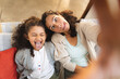 © Wavebreak Media - Mixed race mother and daughter sitting on sofa doing funny faces, taking selfie