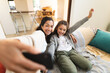 © Wavebreak Media - Mixed race mother and daughter sitting on sofa doing funny faces, taking selfie