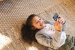 © Wavebreak Media - Smiling mixed race girl lying on carpet using smartphone