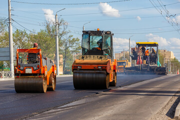 Process of asphalting, asphalt paver machine and two road rollers during road construction works, working on the new road, in summer day