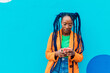 © Image Source RF - Italy, Milan, Woman with braids using smart phone against blue wall