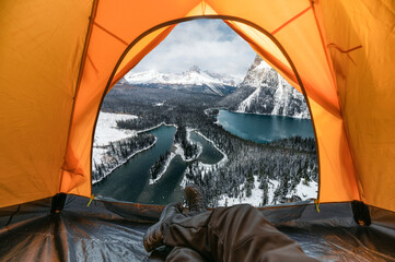 Wall Mural - Traveler man resting and enjoying view of snowy mountain and lake inside a orange tent on winter at national park