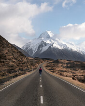Travel lifestyle view of person walking down mountain road leading to Aoraki / Mount Cook National Park, on the South Island of New Zealand.