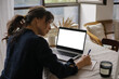 © Anikonaann - View from back of woman using laptop and writing in notebook. Mockup White screen laptop, computer