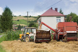 Kombajn nasypuje ziarna pszenicy na przyczepę ciągnika w czasie żniw