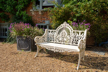 Ornate Iron Metal Vintage Retro Garden Seat, Painted In White Colour, Located In Rural Garden With Planter.