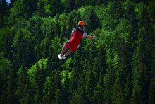 A Young Man Jumped From Bungee Jumping And Now Hangs On A Rope And Films Himself On A Sports Video Camera Against A Blurred Background Of A Green Forest