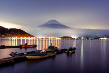 View Of Mount Fuji Covered With Snow At Sunset During A Foggy Day With Boats Along Lake Kawaguchi In Foreground, Japan.