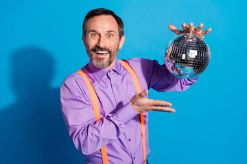 Poster - Photo of cheerful mature man happy positive smile show hand disco ball party isolated over blue color background