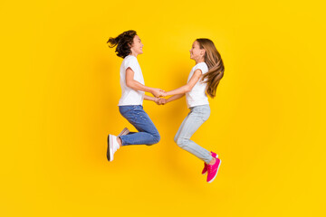 Sticker - Full length body size view of two nice cheerful carefree kids jumping holding hands isolated over bright yellow color background