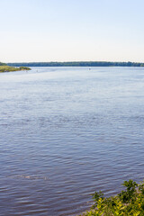 A wide river flows along between two banks under a blue sky