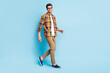 Photo of excited cute young guy dressed plaid shirt spectacles smiling walking isolated blue color background