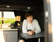 © Enrique - Photo of an attractive young female using her phone while sitting in a sofa inside of a campervan