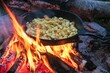 fried potatoes in cubes  with bacon and onions in an iron cast pan over open fire, outdoor cooking