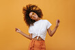 Emotional curly girl in light t-short playing her hair on isolated backdrop. Joyful woman in glasses poses on yellow background..