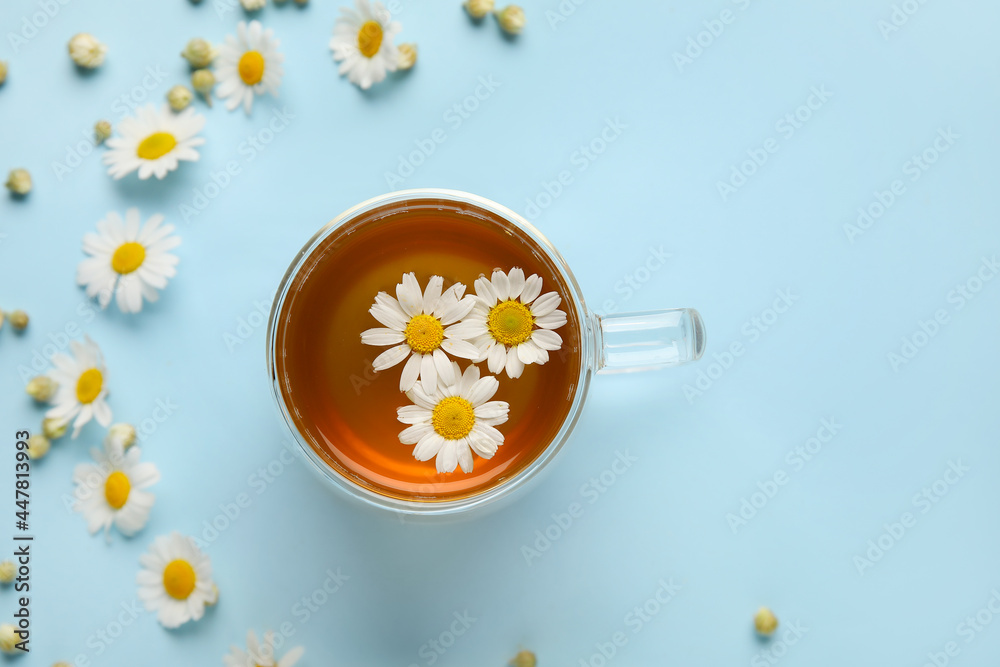Composition with cup of chamomile tea and flowers on color background