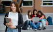 © Bangkok Click Studio - Close up young attractive female college students holding document files smiling at camera with blurry university campus and other students. Outdoor. Concept for education, college students life