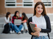 © Bangkok Click Studio - Close up young attractive female college students holding document files smiling at camera with blurry university campus and other students. Outdoor. Concept for education, college students life