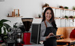 © Natee Meepian - Cheerful young asian woman owner holding digital tablet while standing in her cafe, young entrepreneur conceptual