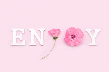 Wall Mural - Enjoy. Motivational quote from white letters and beauty natural flowers on pink background. Creative concept inspirational quote of the day