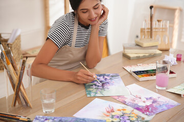 Canvas Print - Young woman drawing flowers with watercolors at table indoors, focus on painting