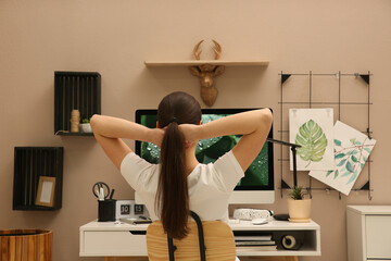 Canvas Print - Woman sitting at white desk with computer near beige wall, back view. Interior design